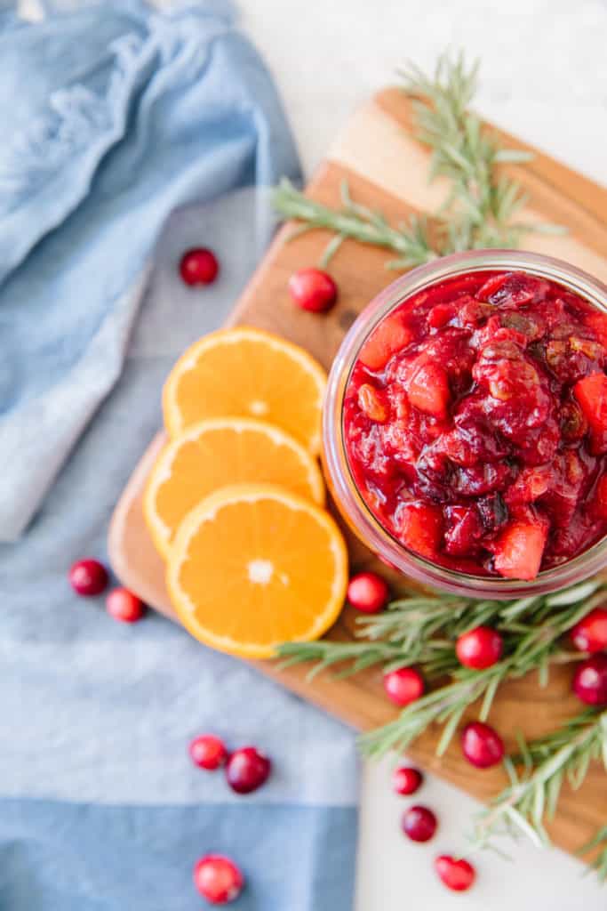 Cranberry chutney on a wooden tray for serving with rosemary and fresh cranberries for garnish